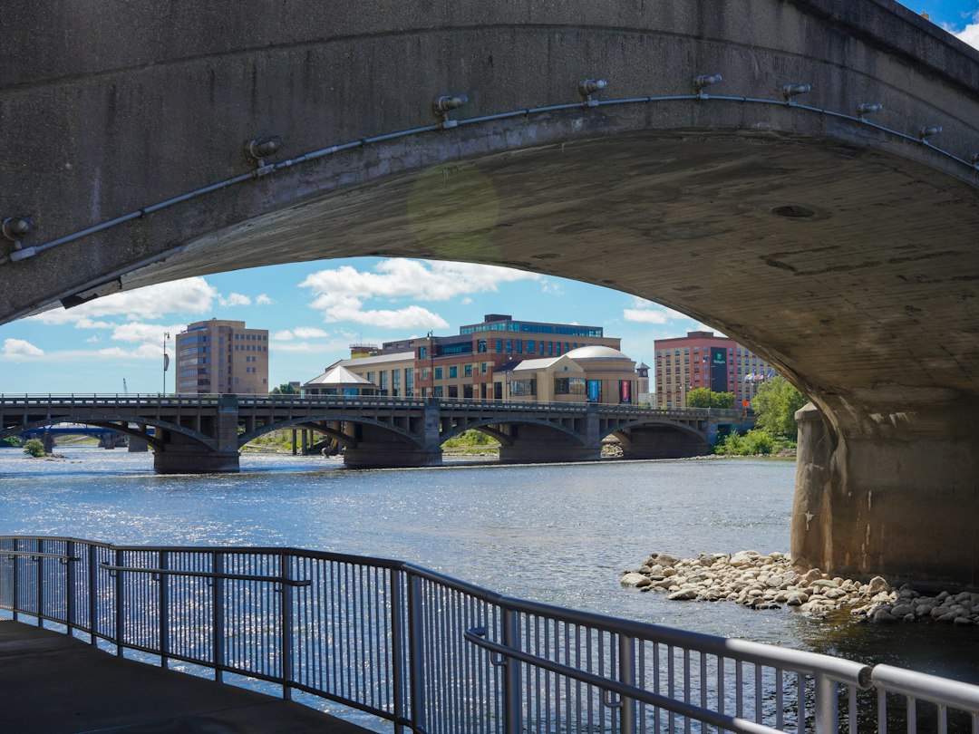 A concrete bridge arch framing a view of a river and city buildings under a blue sky